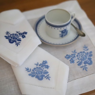 Guardanapos e toalha de linho com bordado azul ao lado de chávena e prato de porcelana com padrão azul