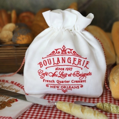 Saco branco com bordado vermelho de padaria numa mesa com pão e faca