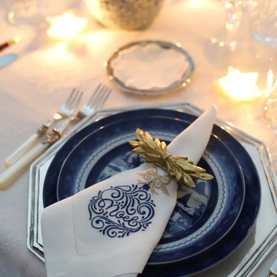 Prato azul decorado com guardanapo branco bordado e anel dourado num ambiente iluminado
