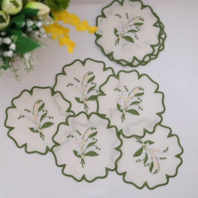Toalhetes brancos bordados com flores e bordas verdes, junto a flores amarelas e verdes.