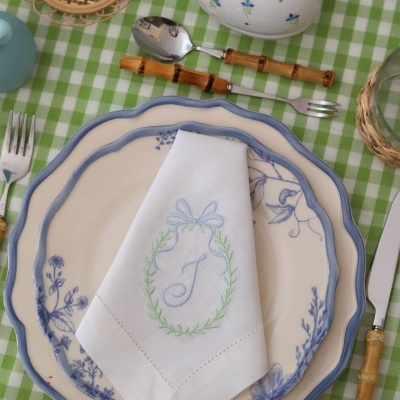 Conjunto de loiça floral azul com guardanapo bordado e talheres com cabo de bambu em mesa xadrez verde e branca.