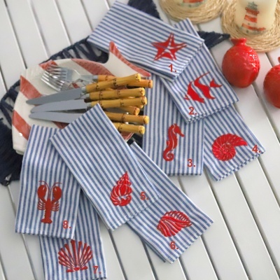 Panos de prato listrados azuis e brancos com bordados vermelhos de motivos marinhos em mesa branca.