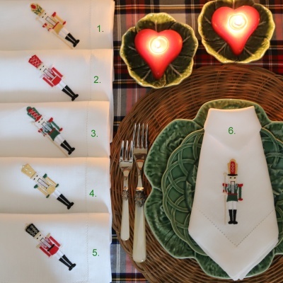 Mesa posta com guardanapos brancos bordados com soldadinhos de chumbo e pratos verdes sobre tabuleiro de vime