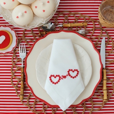 Mesa posta com pratos, talheres de madeira, guardanapo branco com corações vermelhos e cupcakes com corações vermelhos