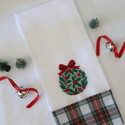 Toalha branca com bordado natalício e padrão xadrez na bainha.