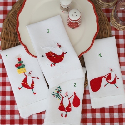 Quatro guardanapos de tecido branco com bordados de Natal de Pai Natal em diferentes poses sobre uma toalha de mesa xadrez vermelha e branca.