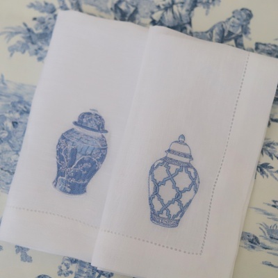 Toalhas brancas com bordado azul de frascos decorativos em fundo de tecido azul e branco com padrão floral