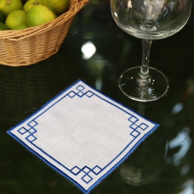 Guardanapo branco com bordas azuis sobre mesa de vidro com taça e cesta de frutas