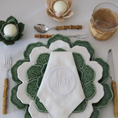 Conjunto de loiça com pratos em forma de folhas, guardanapo bordado, talheres com cabo bambu, castiçais com velas e copo com suporte de verga