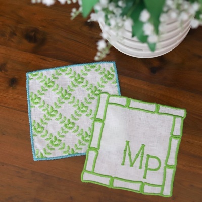 Dois panos de prato brancos com bordados verdes em padrões distintos sobre uma mesa de madeira.