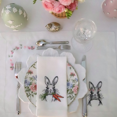 Conjunto de loiça com prato decorado floral, guardanapo branco bordado com coelho, talheres prateados e copo de vidro