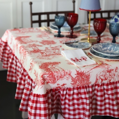 Mesa posta com toalha de mesa vermelha e branca xadrez e estampa vermelha, pratos azuis e brancos, copos coloridos e candelabro