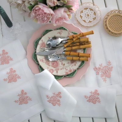 Conjunto de pratos e talheres com cabos de bambu sobre toalhas brancas bordadas com flores cor-de-rosa
