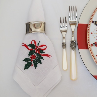 Guardanapo branco bordado com azevinho, anel metálico, dois garfos com cabos decorativos e prato com soldados de chumbo