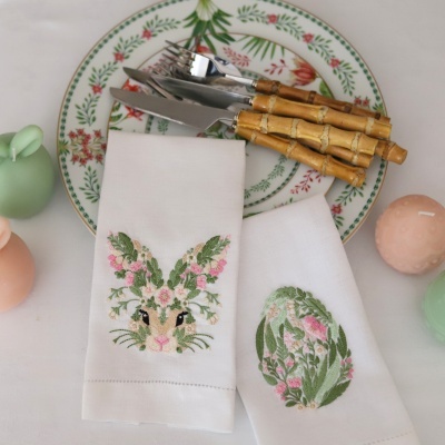 Guardanapos brancos bordados com coelho e padrão floral, prato com padrão floral, talheres com cabo de bambu e velas coloridas