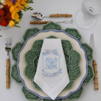 Conjunto de pratos verdes com padrão de folhas, talheres com cabo bambu e guardanapo branco bordado