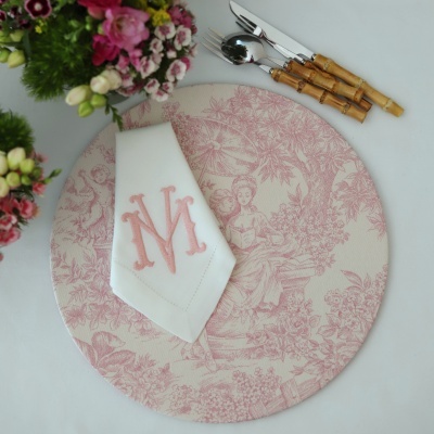 Prato decorativo rosa com ilustração clássica, guardanapo branco com monograma rosa e talheres de cabo de madeira