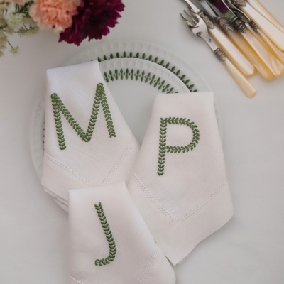 Guardanapos brancos com letras bordadas em verde sobre pratos brancos decorados com padrão verde