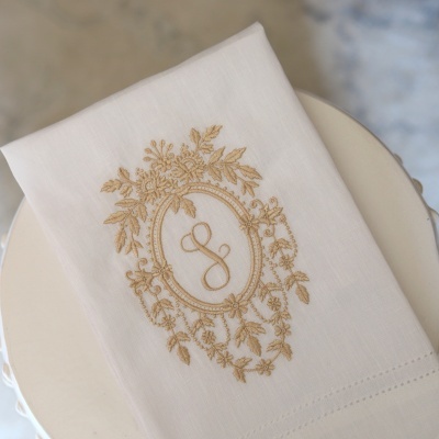Toalha branca com bordado dourado de flores e letra S