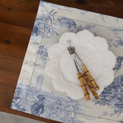 Toalha de mesa branca com estampado azul, prato branco em forma de folha e garfos com cabo de bambu