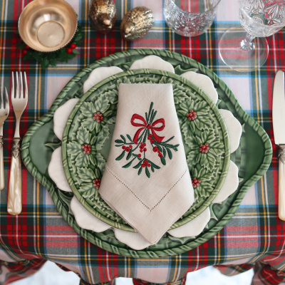 Conjunto de loiça decorativa de Natal com pratos, guardanapo bordado e copo de cristal sobre toalha quadriculada