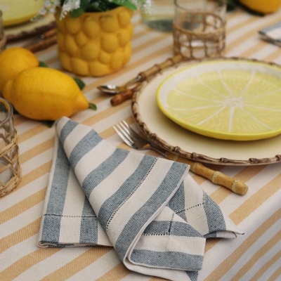 Mesa posta com toalha de riscas, guardanapo, prato decorativo, limões e copo com suporte de rattan