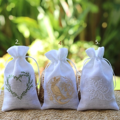 Três saquinhos de tecido branco bordados com cordão em cima de superfície rústica