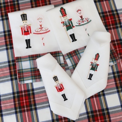 Quatro guardanapos brancos com bordados de soldados e bailarinas coloridos sobre fundo xadrez