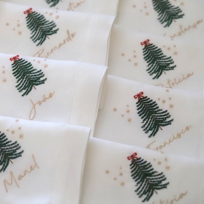 Guardanapos brancos bordados com árvores de Natal verdes com laços vermelhos e nomes em dourado