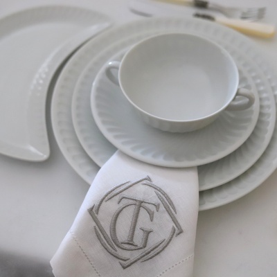 Conjunto de loiça branca com padrão ondulado e guardanapo bordado com letras TG
