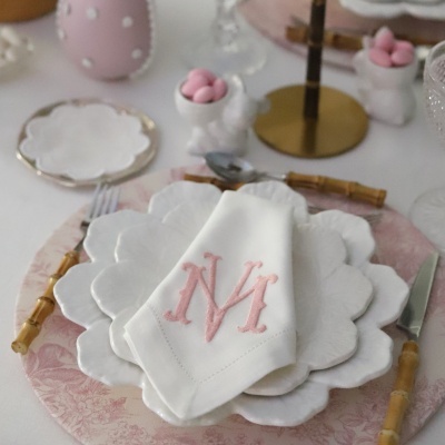 Mesa posta com pratos brancos em forma de flor e guardanapo com monograma NM