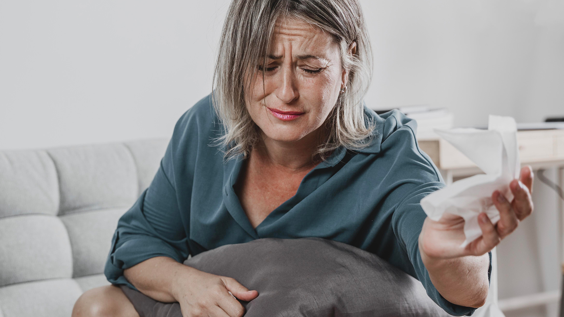 Mulher sentada no sofá a segurar lenço de papel e almofada