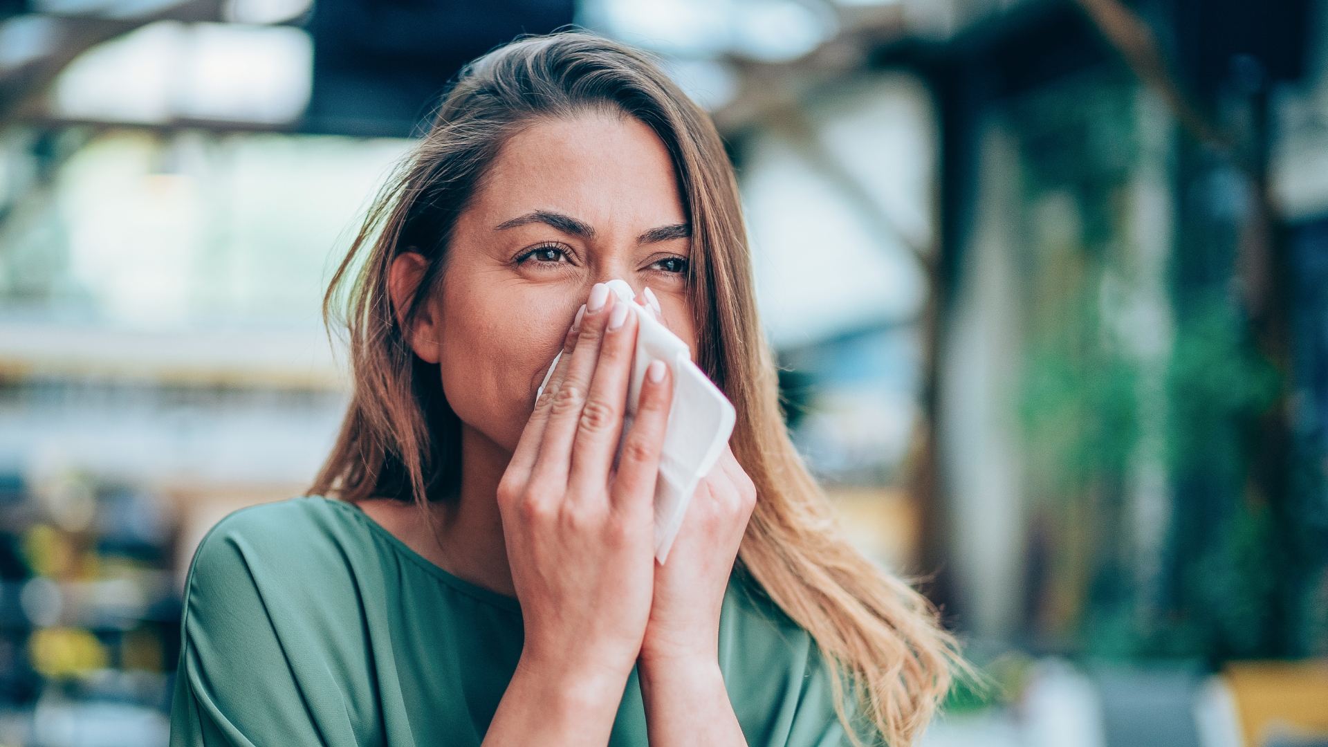 Mulher segura lenço de papel perto do nariz em ambiente interior