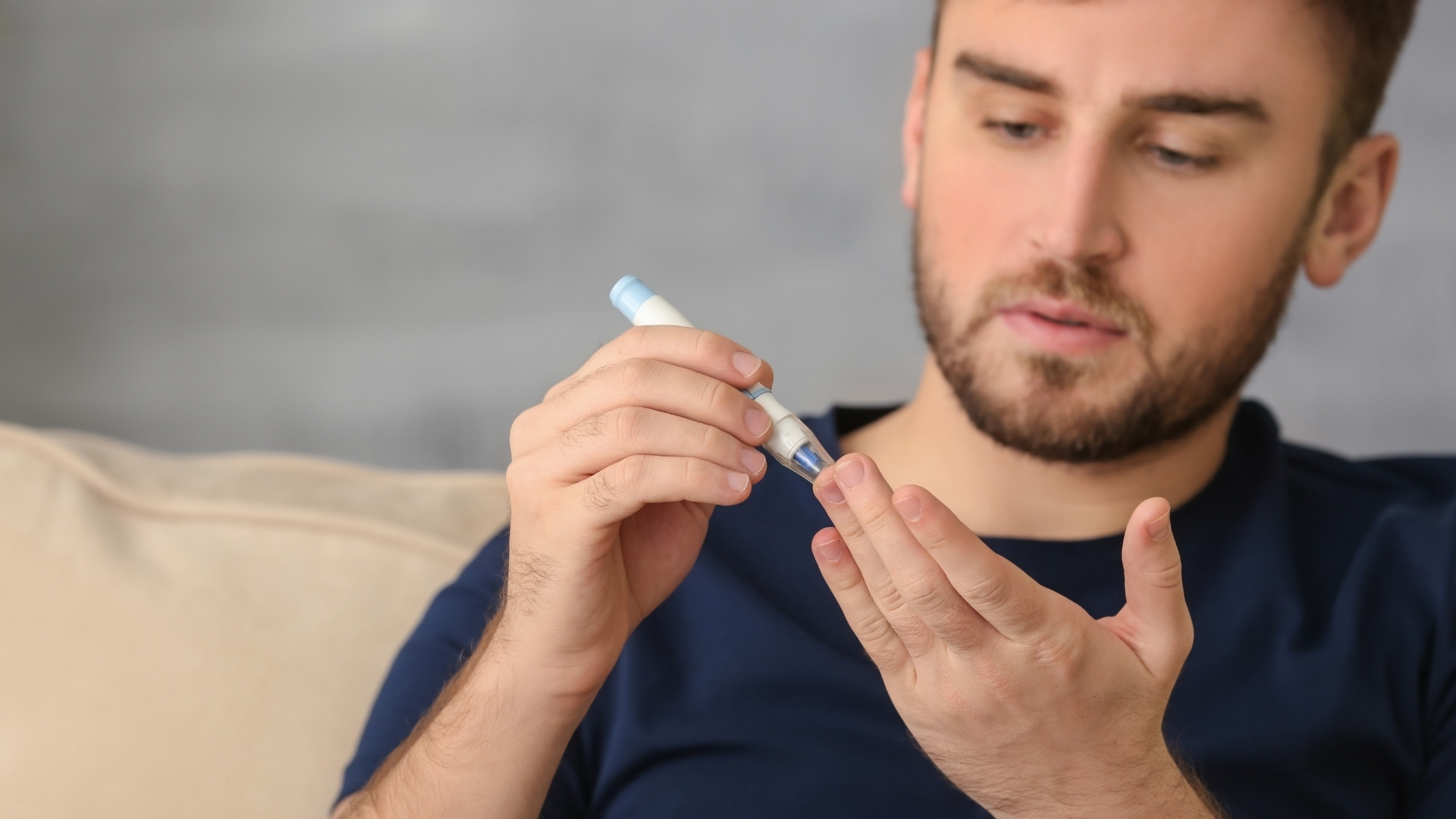 Homem a medir glicose no dedo com dispositivo azul e branco sentado no sofá