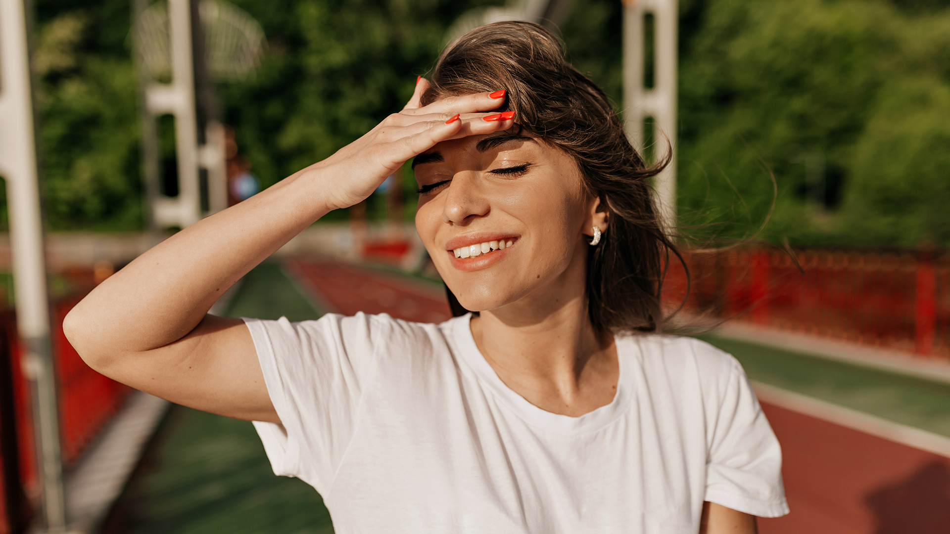 Mulher com camisa branca e unhas vermelhas a tapar-se do sol em área exterior