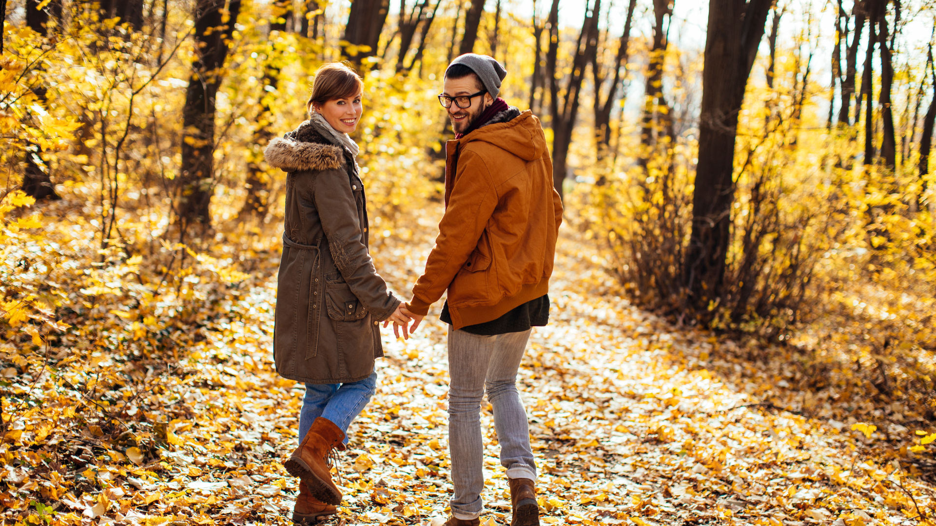 Casal vestido para outono caminhando numa floresta com folhas caídas no chão