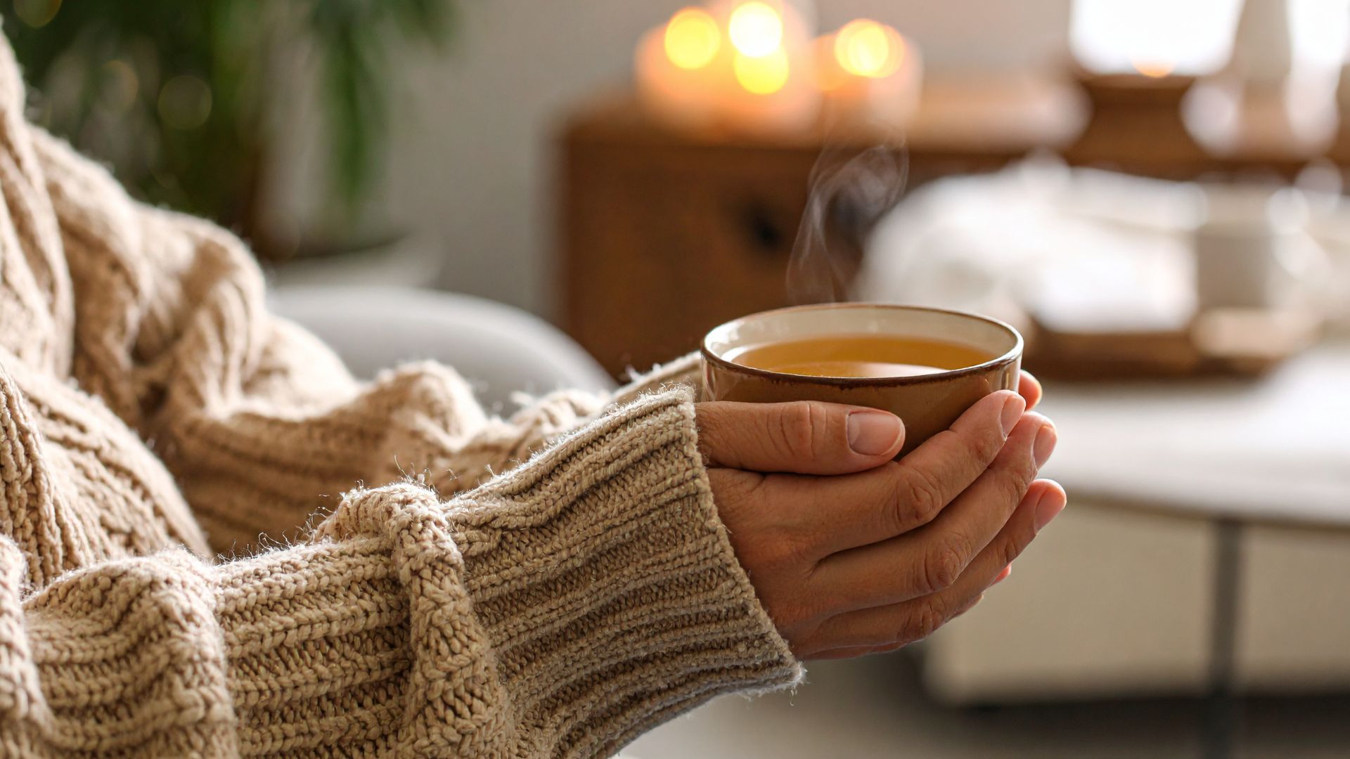 Caneca cerâmica castanha com chá quente em mãos com camisola castanha clara