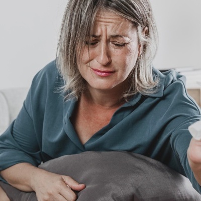 Mulher sentada no sofá a segurar lenço de papel e almofada