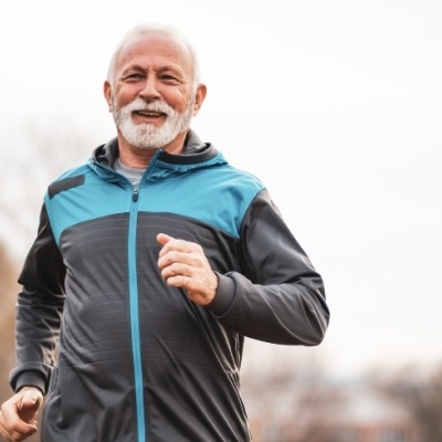 Homem idoso a correr com casaco desportivo cinzento e azul ao ar livre