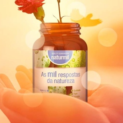 Frasco de vidro castanho com etiqueta Naturmil segurado por mão em fundo de pôr do sol