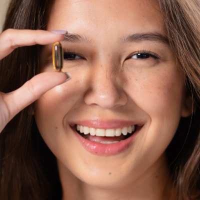 Mulher segurando cápsula transparente âmbar perto do rosto, sorrindo