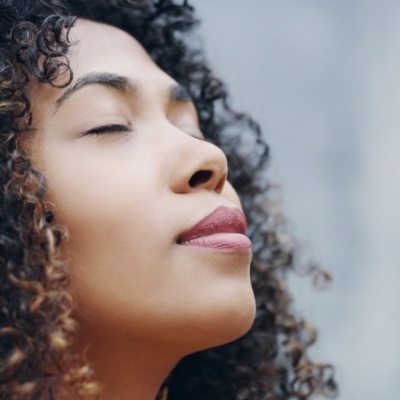 Mulher jovem com cabelo cacheado e olhos fechados num ambiente desfocado