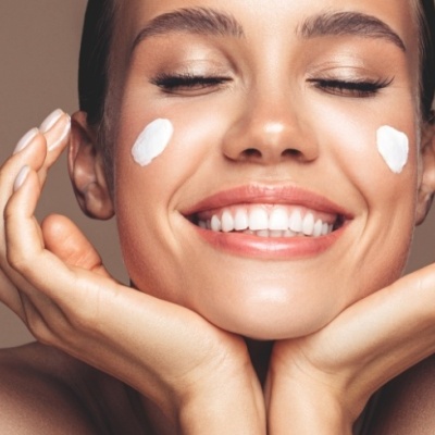 Mulher feliz com creme aplicado nas bochechas, fundo castanho claro