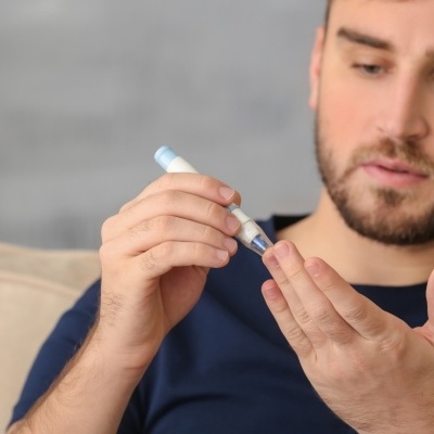 Homem a medir glicose no dedo com dispositivo azul e branco sentado no sofá