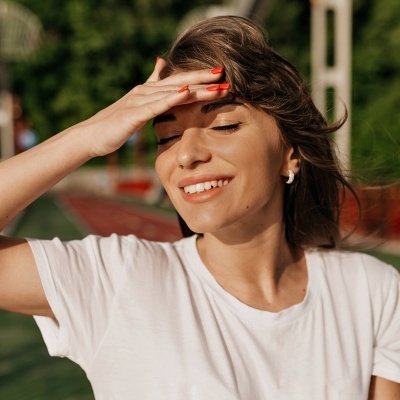 Mulher com camisa branca e unhas vermelhas a tapar-se do sol em área exterior