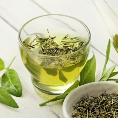Chá verde em folhas secas e chá líquido em copo e bule de vidro com folhas verdes frescas