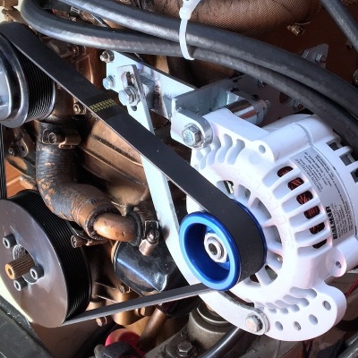 Alternador automóvel branco com correia preta e polias metálicas no compartimento do motor