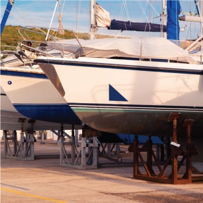 Dois veleiros brancos com detalhes azuis e verdes em suportes metálicos num cais.