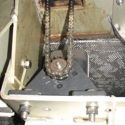 Mecanismo metálico com corrente e roda dentada dentro de estrutura de metal bege