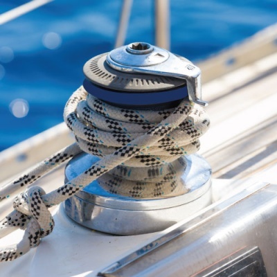 Molinete de vela cromado com corda náutica branca com padrões pretos e azuis num barco